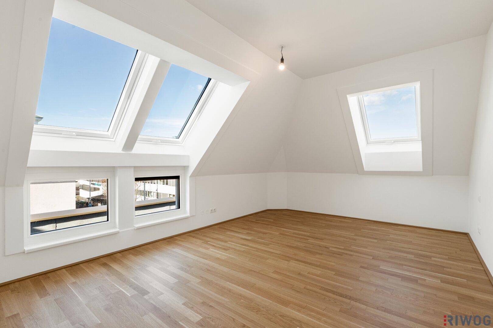 Helles Schlafzimmer im Dachgeschoss mit Parkettboden und mehreren Dachfenstern für viel Licht.
