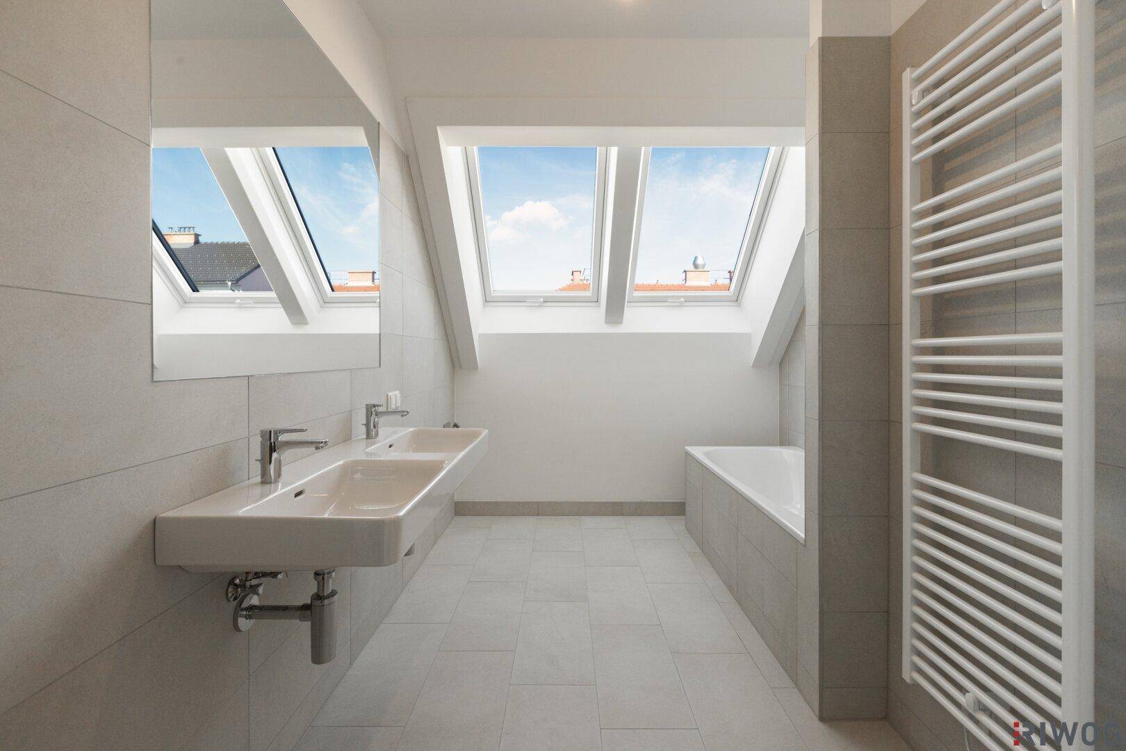 Modernes Badezimmer mit Doppelwaschbecken, Badewanne und Dachfenstern für Tageslicht.