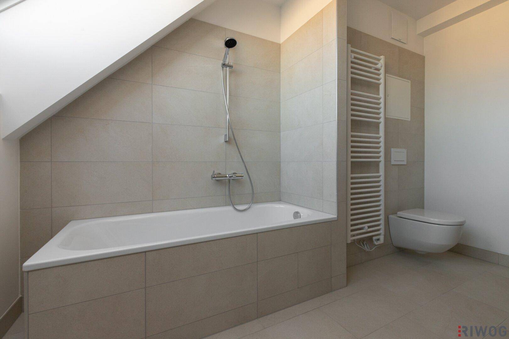 Badezimmer mit integrierter Badewanne, Wand-WC und beheiztem Handtuchhalter.