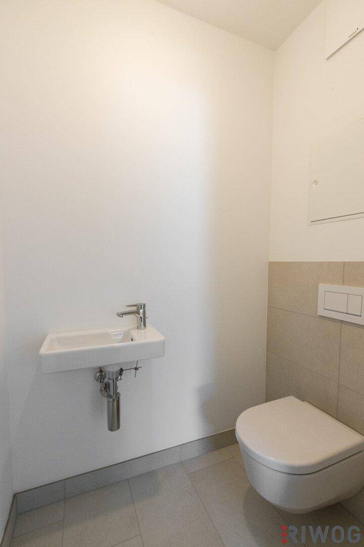 Modernes Gäste-WC mit Wand-WC und kleinem Waschbecken, hell gefliest.