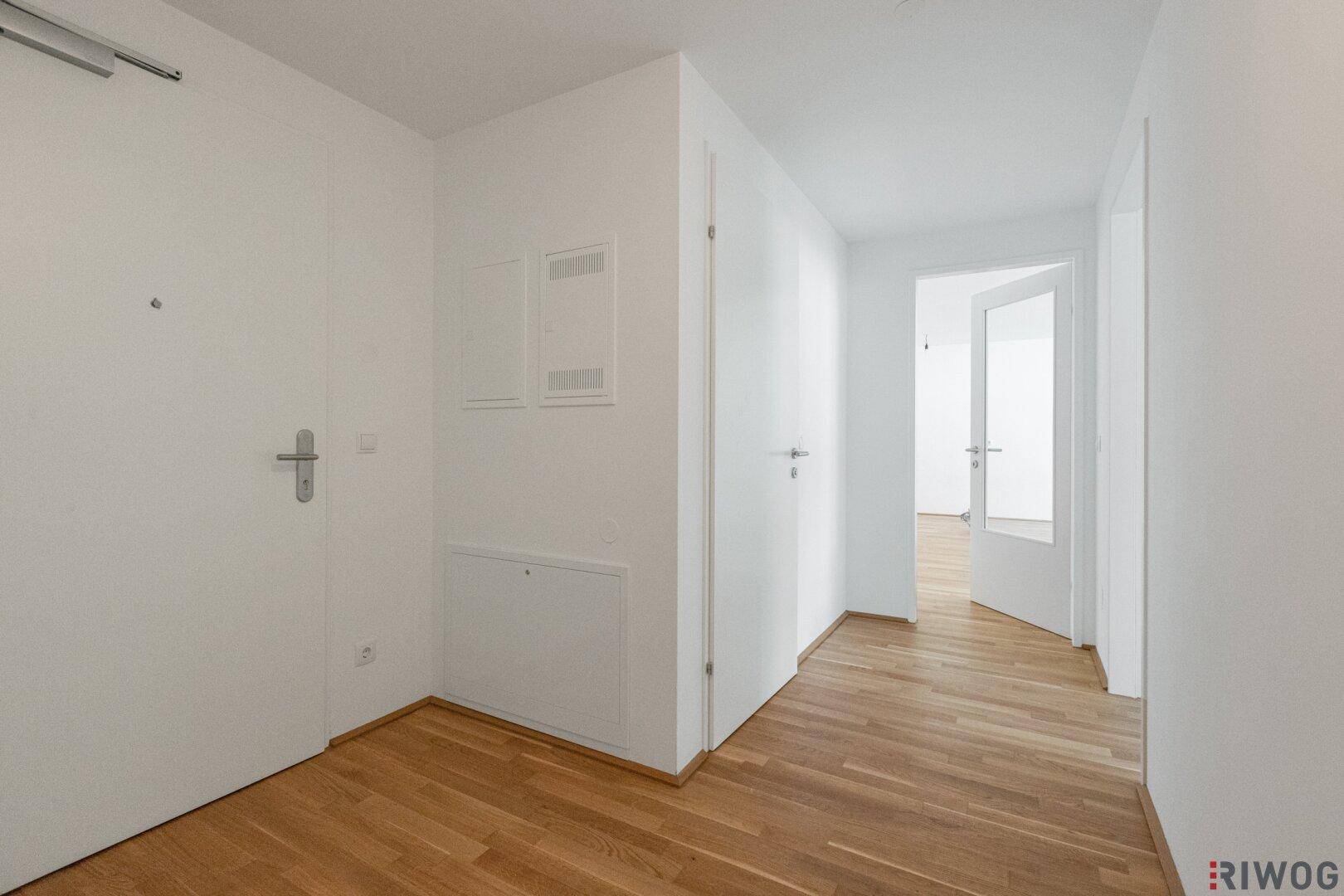 Heller Flur mit Parkettboden und weißen Wänden, führt zu weiteren Räumen.