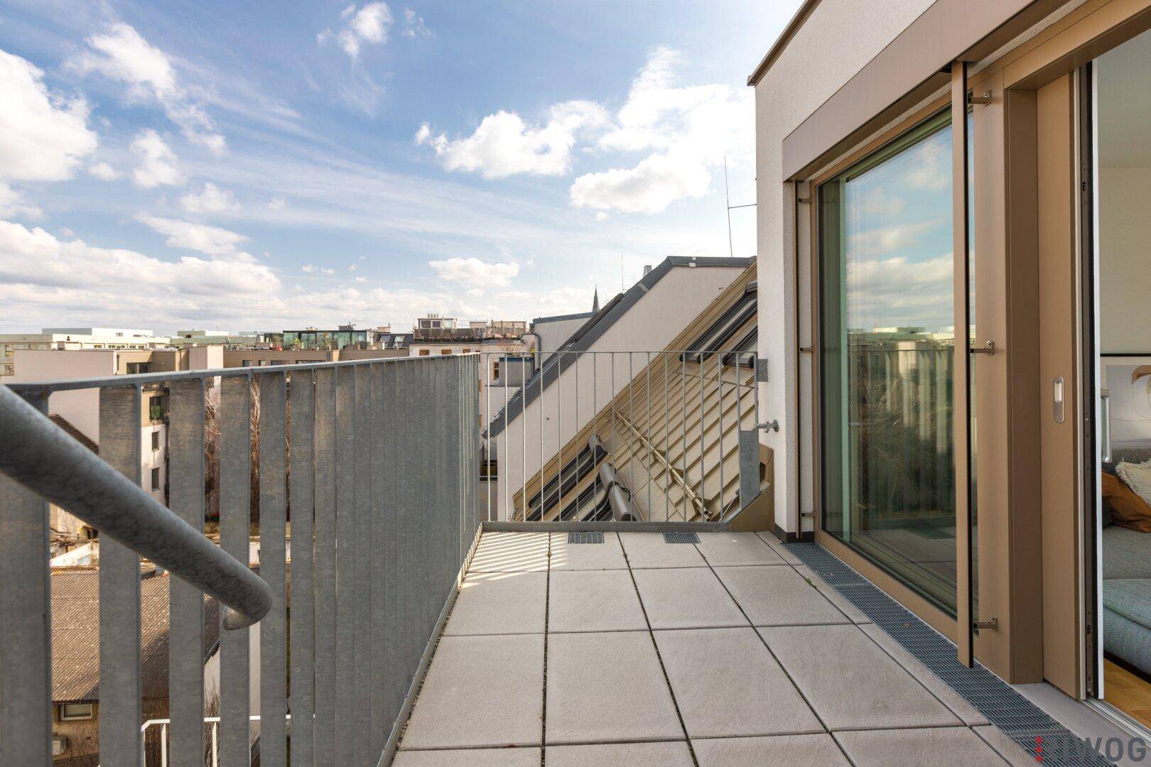 Geräumiger Balkon mit Fliesenboden und weitem Blick über die Stadt an einem sonnigen Tag.