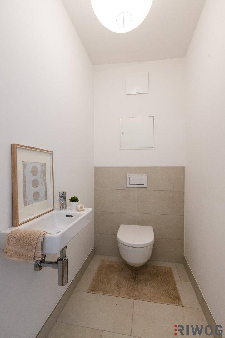 Modernes Gäste-WC mit Wand-WC, kleinem Waschbecken und hellen Fliesen.