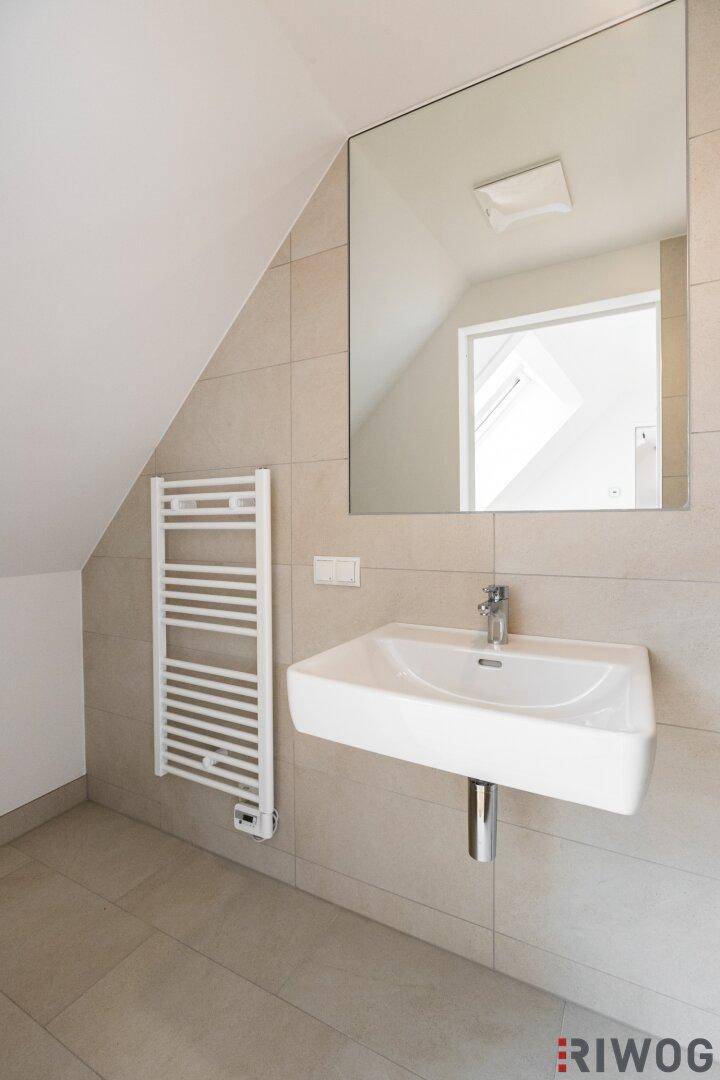 Modernes Badezimmer mit Waschbecken, großem Spiegel und beheiztem Handtuchhalter unter Schrägdecke.