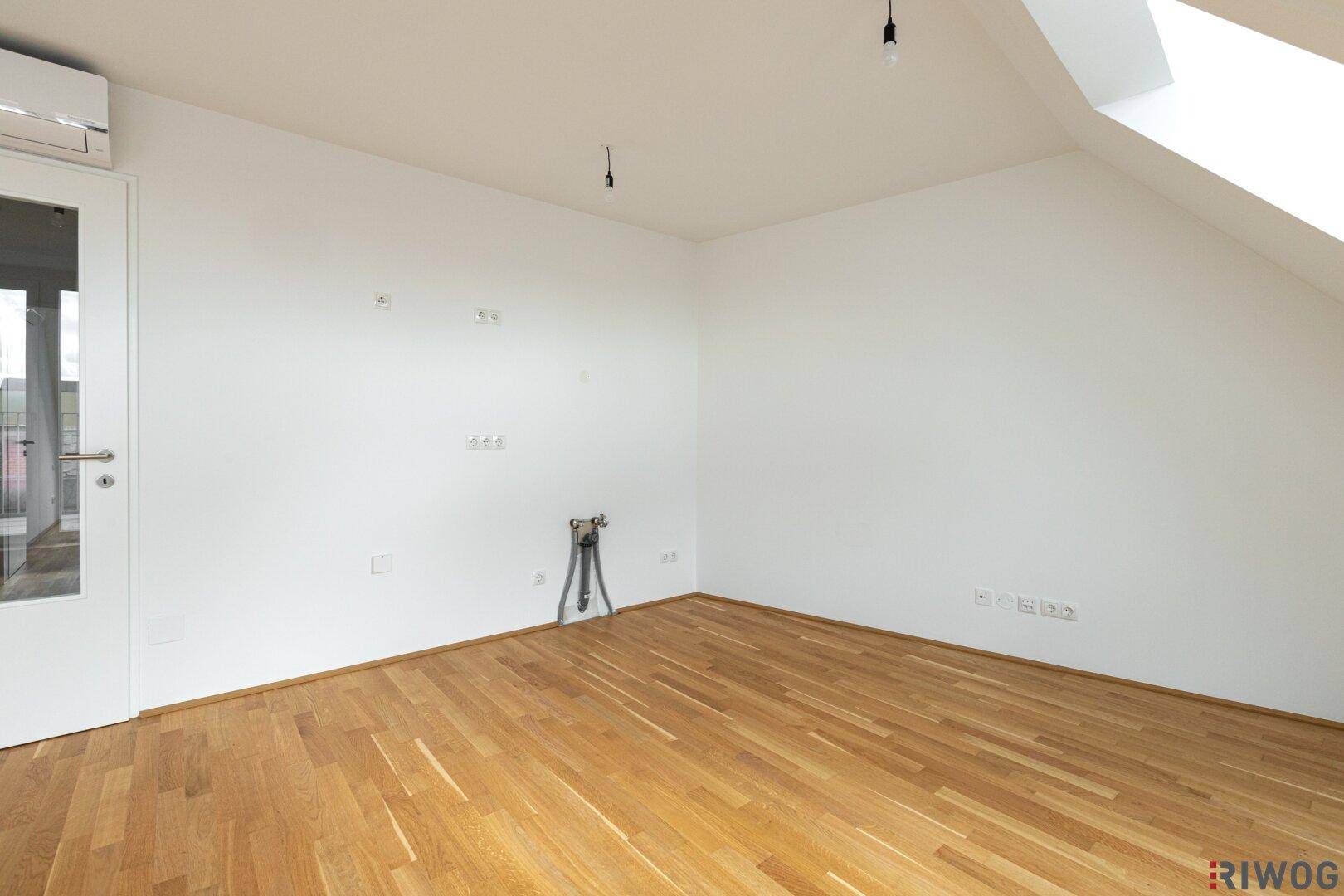 Leerer Raum mit Parkettboden, Dachschräge und Klimaanlage an der Wand.