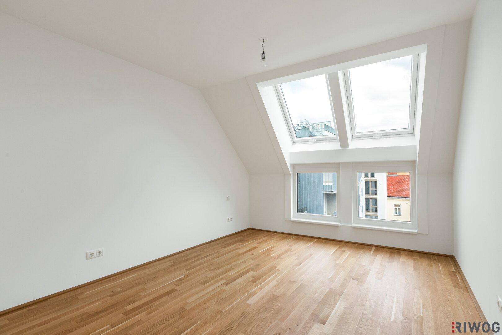 Heller Raum mit Parkettboden, Dachschrägen und großen Dachfenstern.