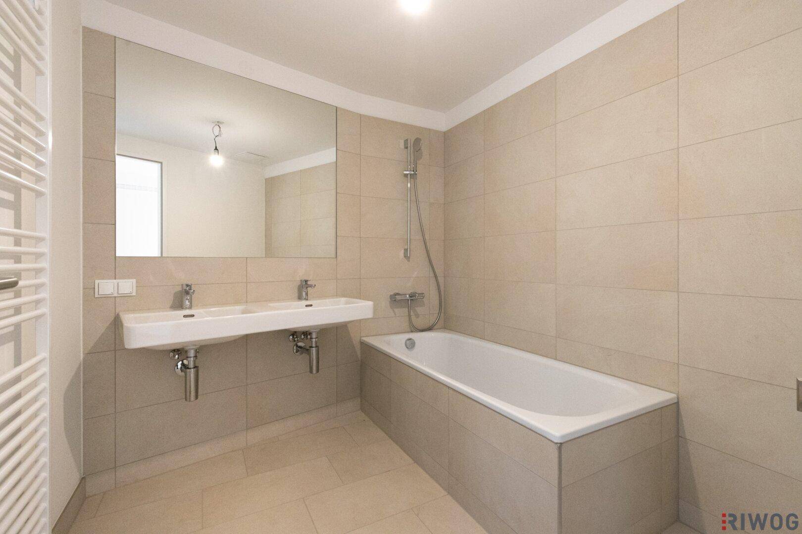 Modernes Badezimmer mit Doppelwaschbecken, Badewanne und hellen Fliesen.
