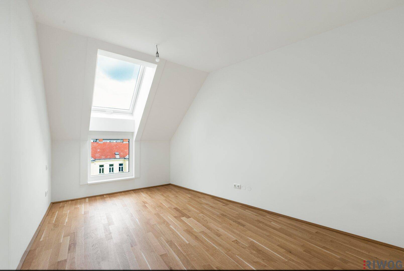 Leerer Raum mit Parkettboden, Dachschräge und einem großen Dachfenster.