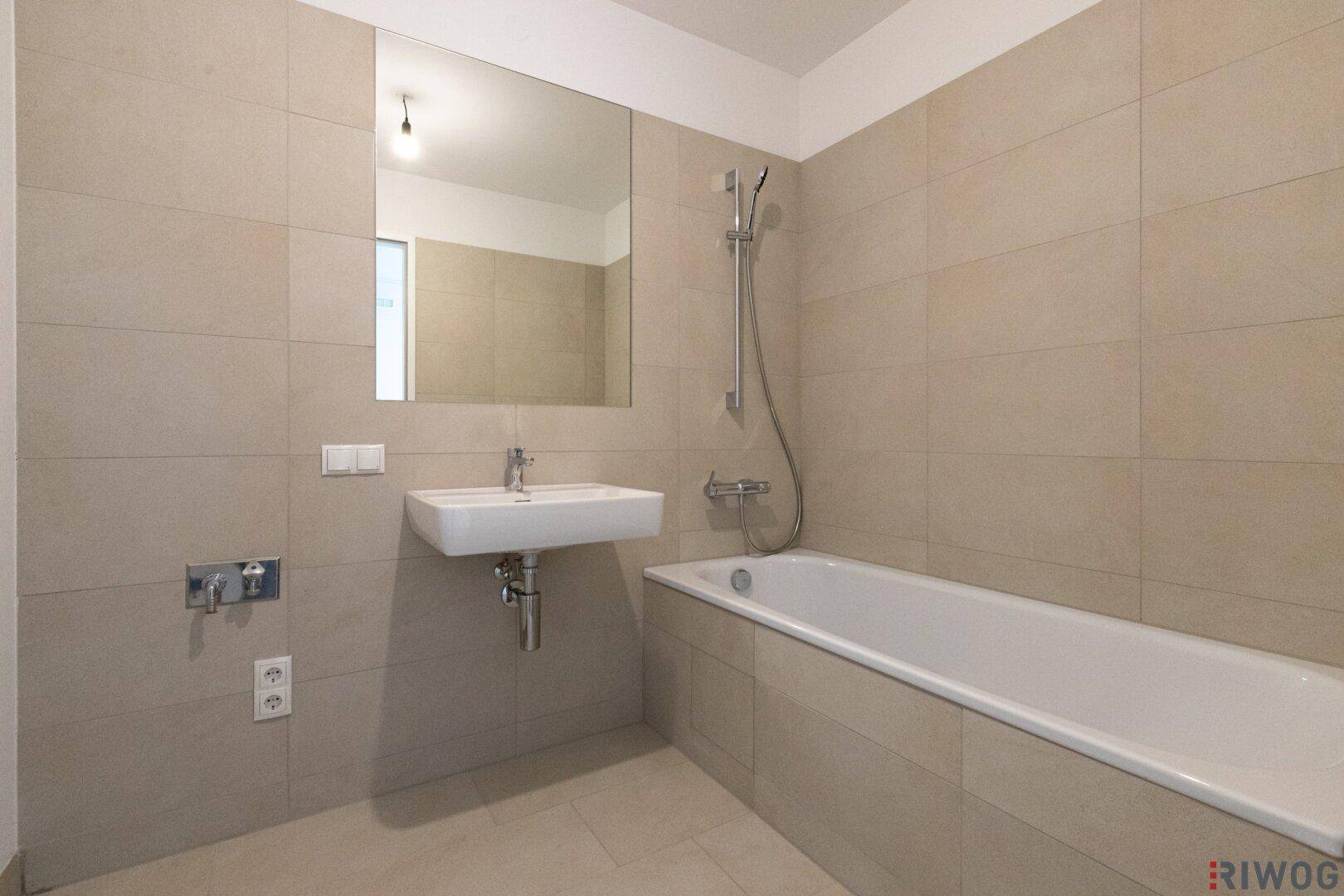 Modernes Badezimmer mit Badewanne, Wandspiegel und beigefarbenen Fliesen.