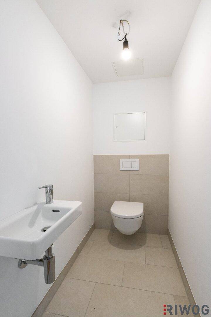 Gäste-WC mit Wand-WC, Waschbecken und hellen Fliesen.
