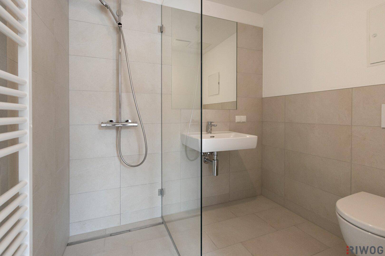 Modernes Badezimmer mit ebenerdiger Dusche, Einzelwaschbecken und beheiztem Handtuchhalter.