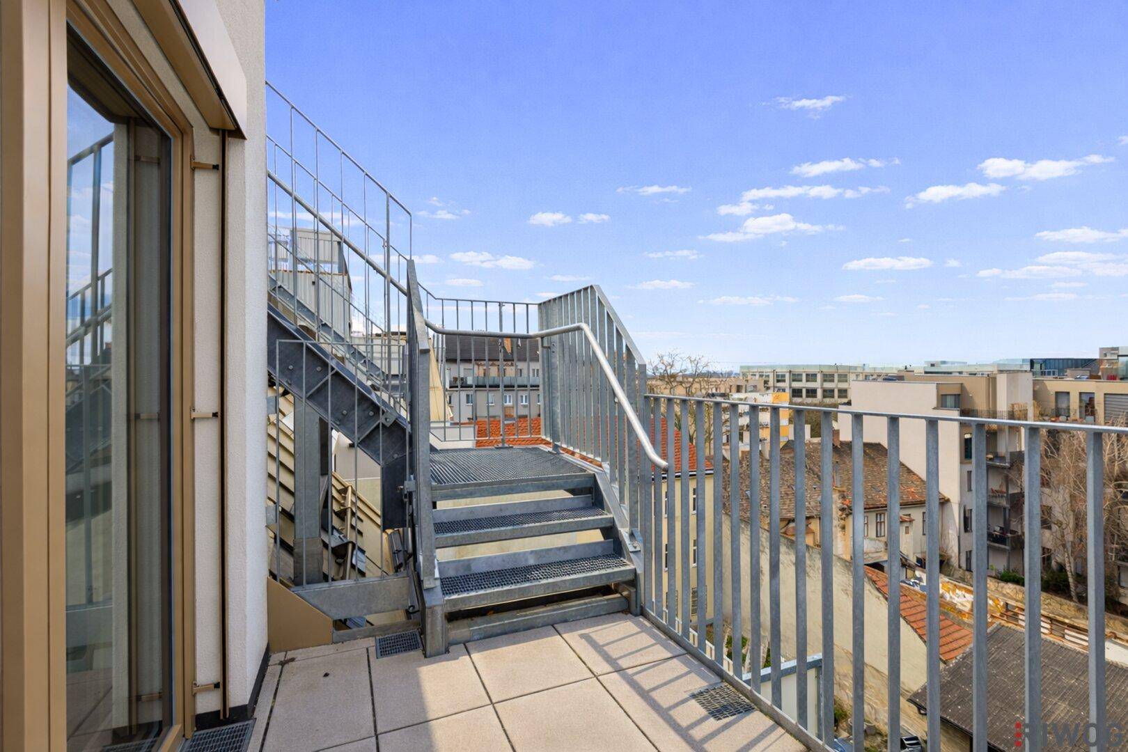 Balkon mit Metallgeländer und Treppe, die zu einer oberen Dachterrasse führt.