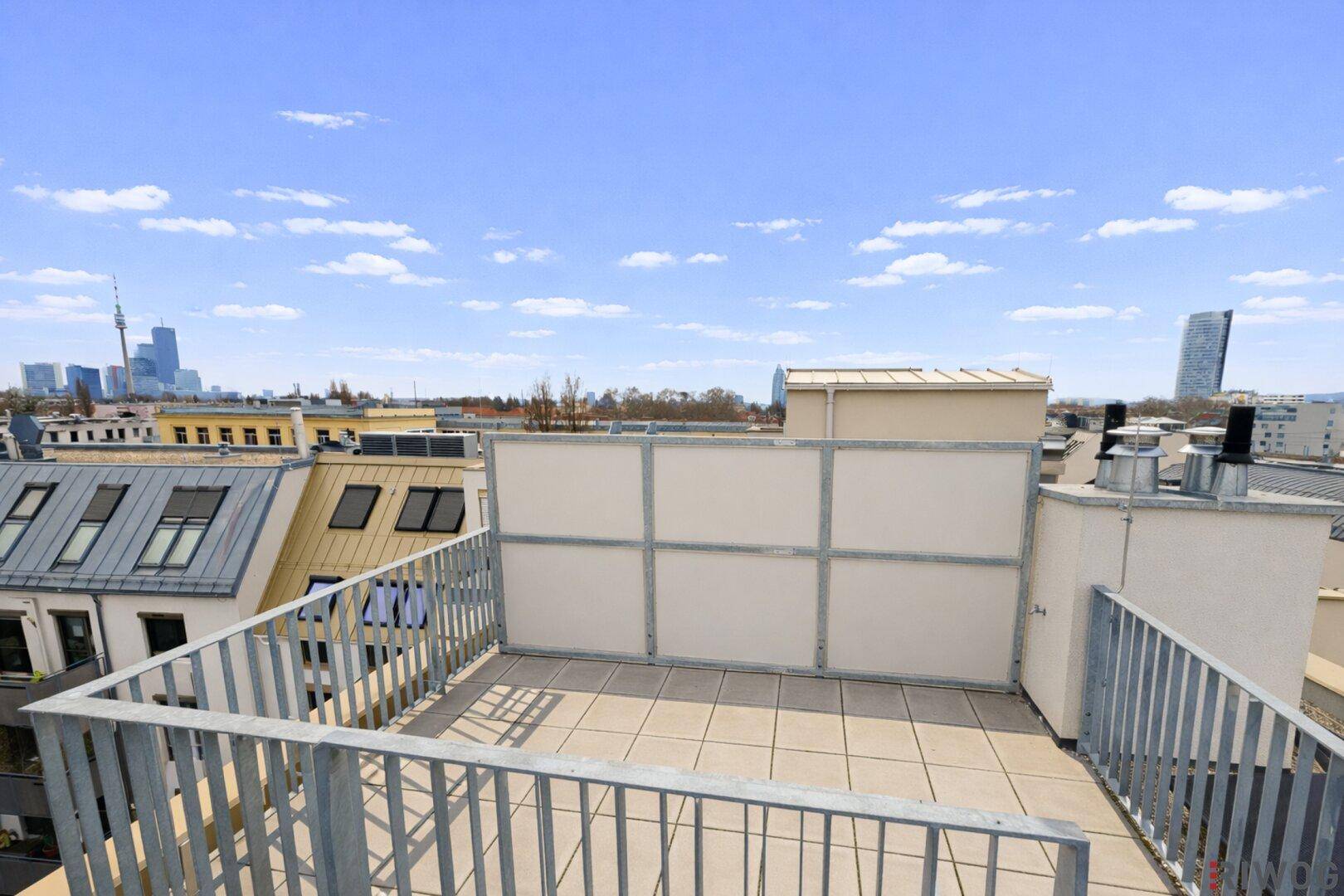 Unmöblierte Dachterrasse mit Fliesenboden und weitem Blick über die Stadt.