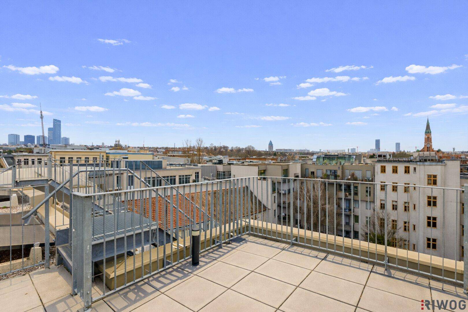 Geräumige Dachterrasse mit Fliesenboden und weitem Blick über die Stadt an einem sonnigen Tag.