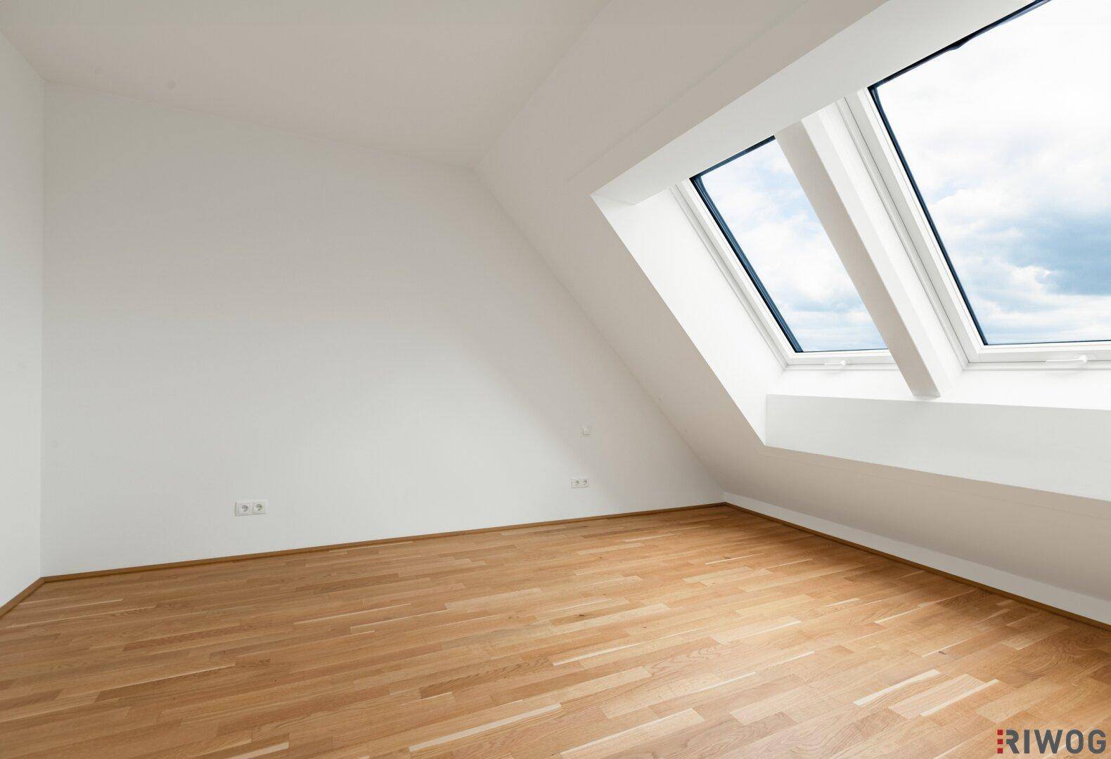 Helles Schlafzimmer im Dachgeschoss mit Parkettboden und großen Dachfenstern.