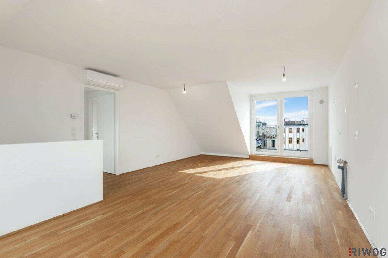 Lichtdurchfluteter Wohnraum mit Parkettboden, Dachschräge und Zugang zu einem französischen Balkon.