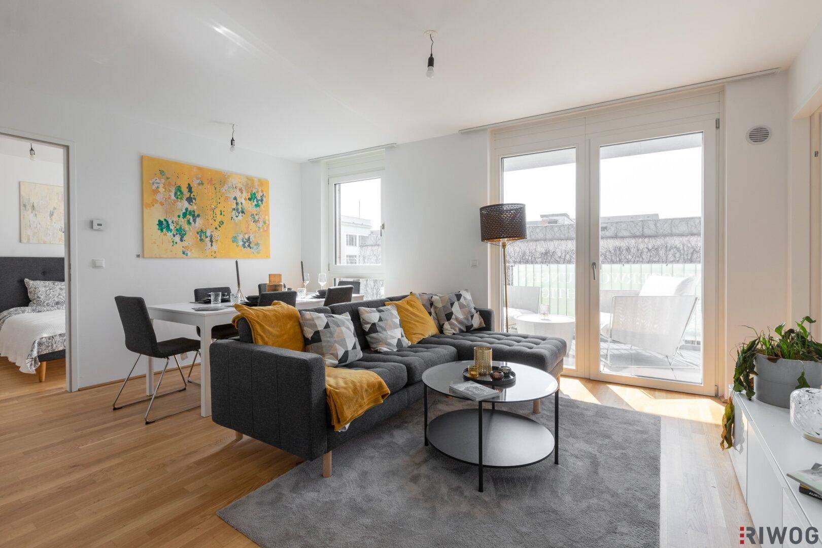 Helles Wohnzimmer mit modernem Sofa, Esstisch und Zugang zum Balkon.