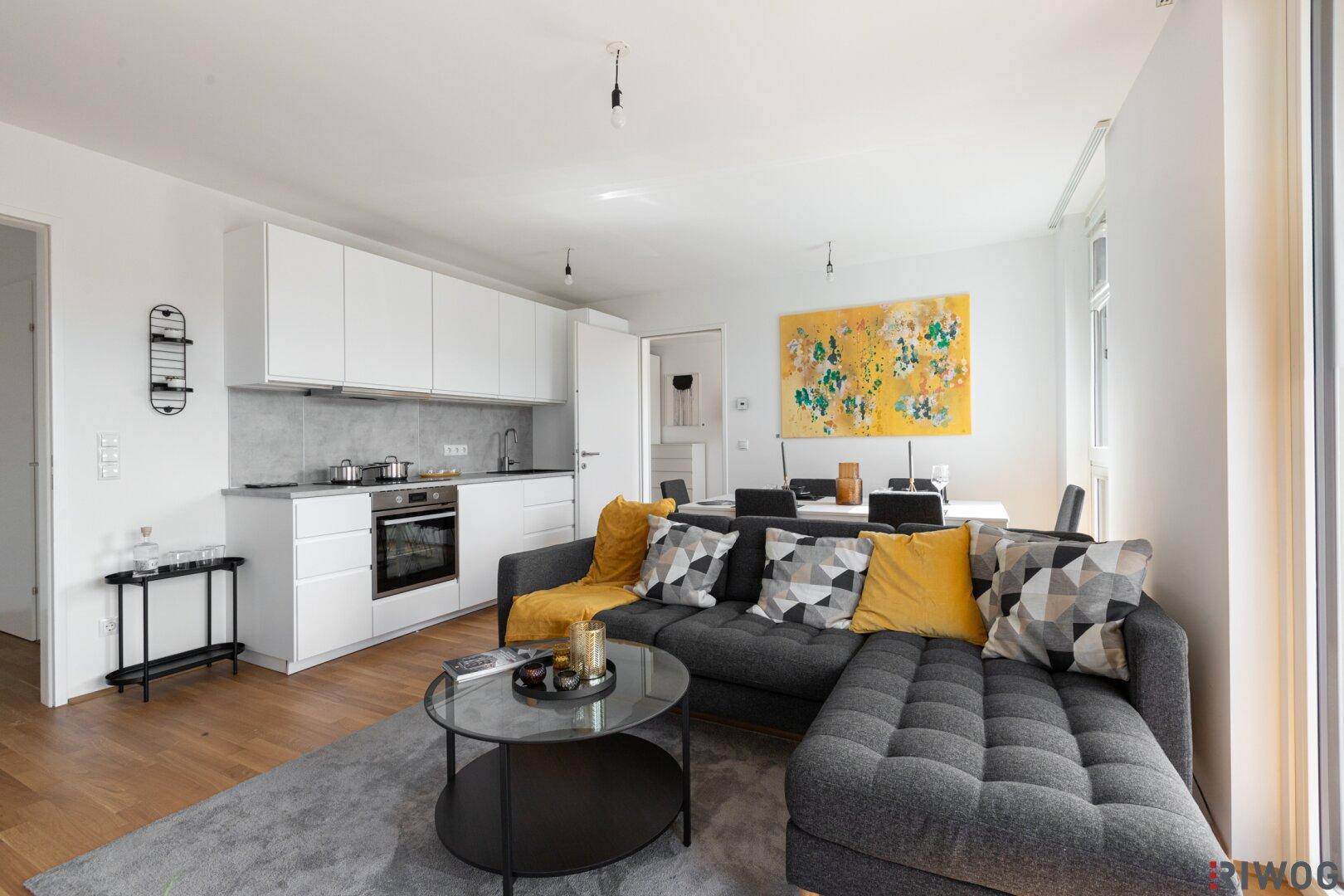 Offener Wohnbereich mit integrierter Küche, modernem Sofa und Holzboden.