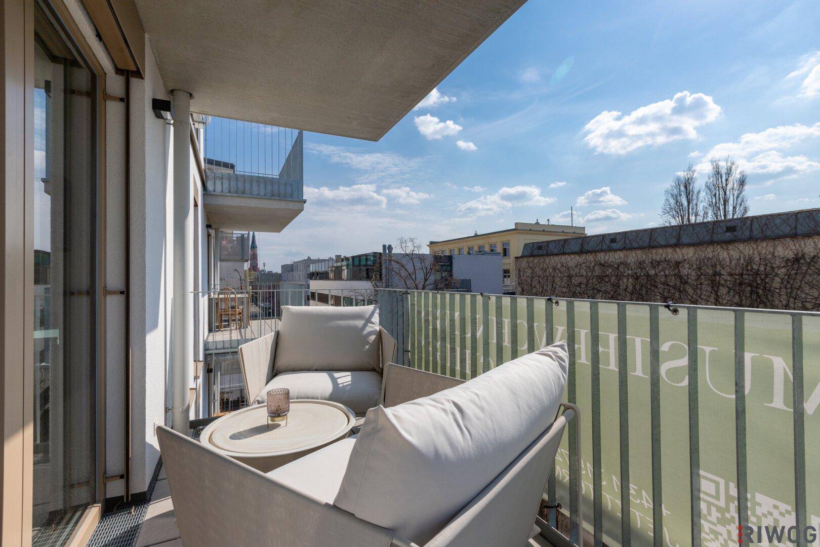 Sonniger Balkon mit bequemen Sitzmöbeln und Blick auf die umliegenden Gebäude.