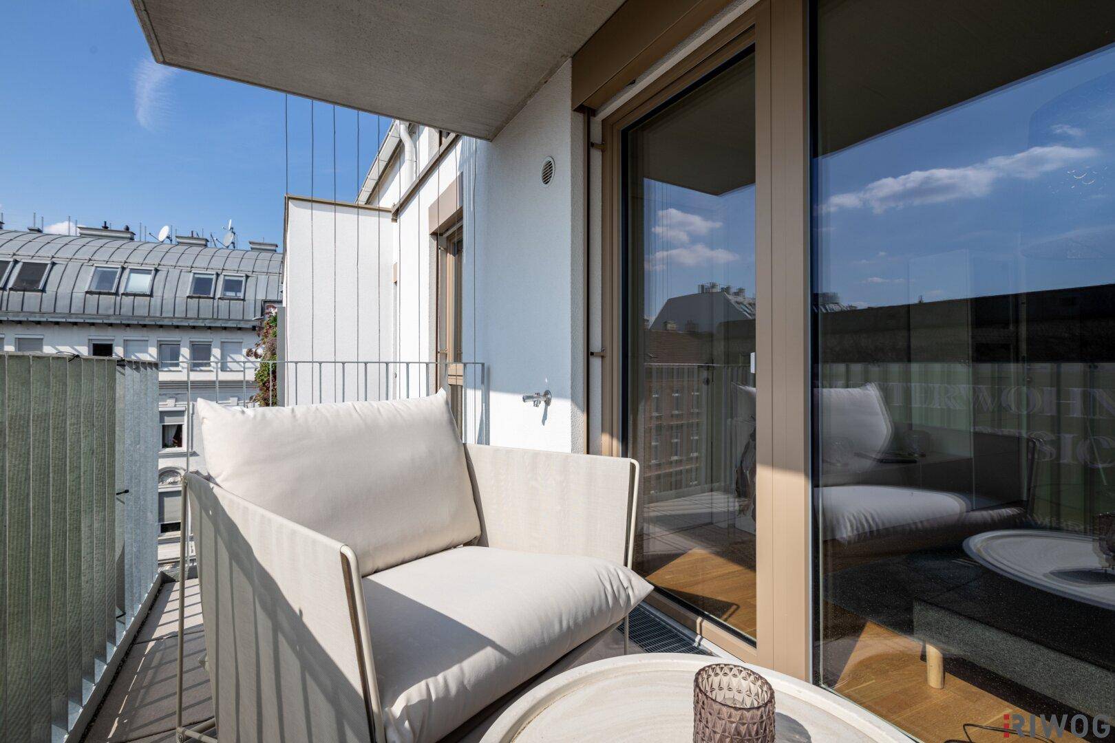 Heller Balkon mit modernen Sitzmöbeln und Blick auf die Dächer der Stadt.