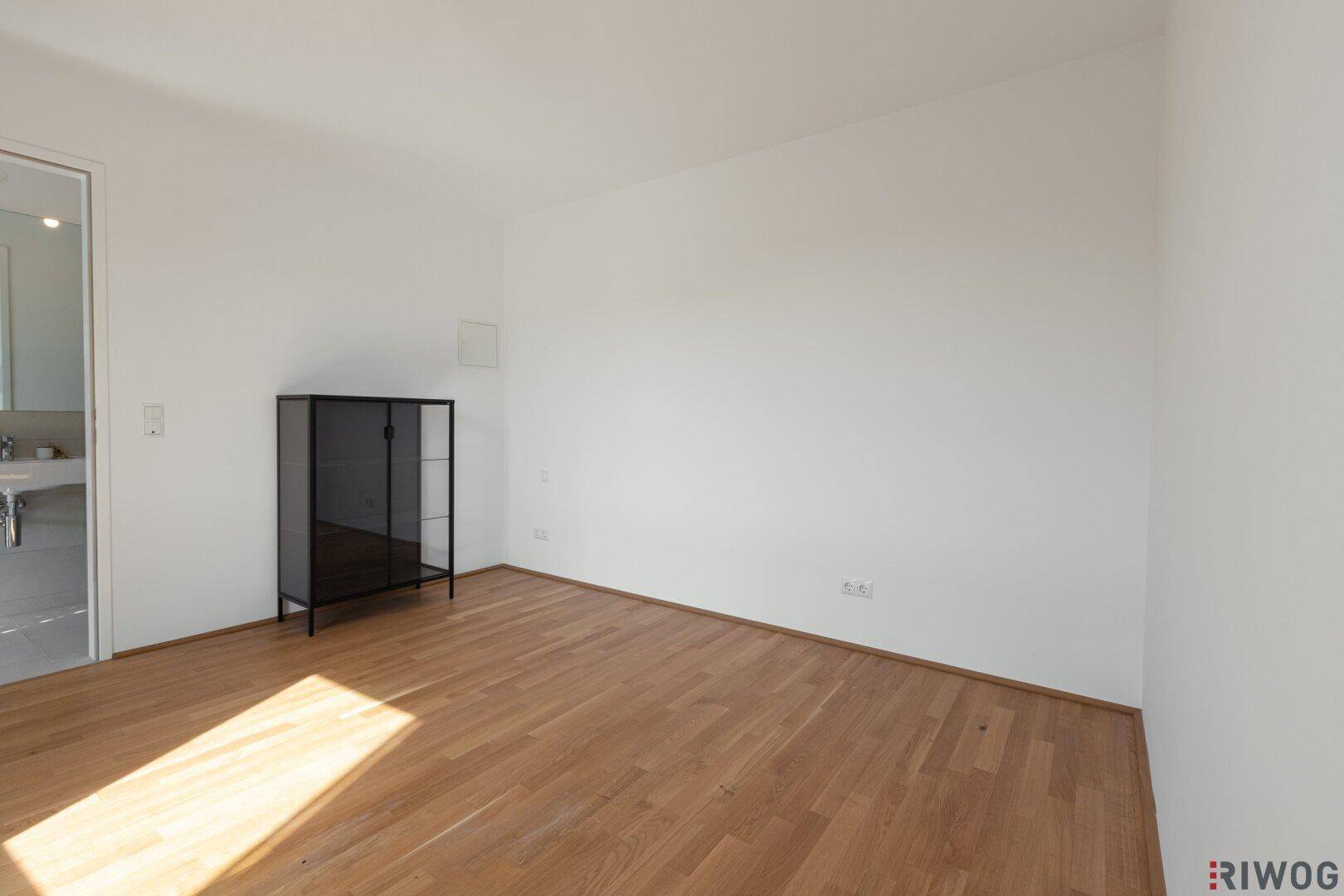 Leeres Schlafzimmer mit Holzboden und Zugang zu einem modernen Badezimmer.