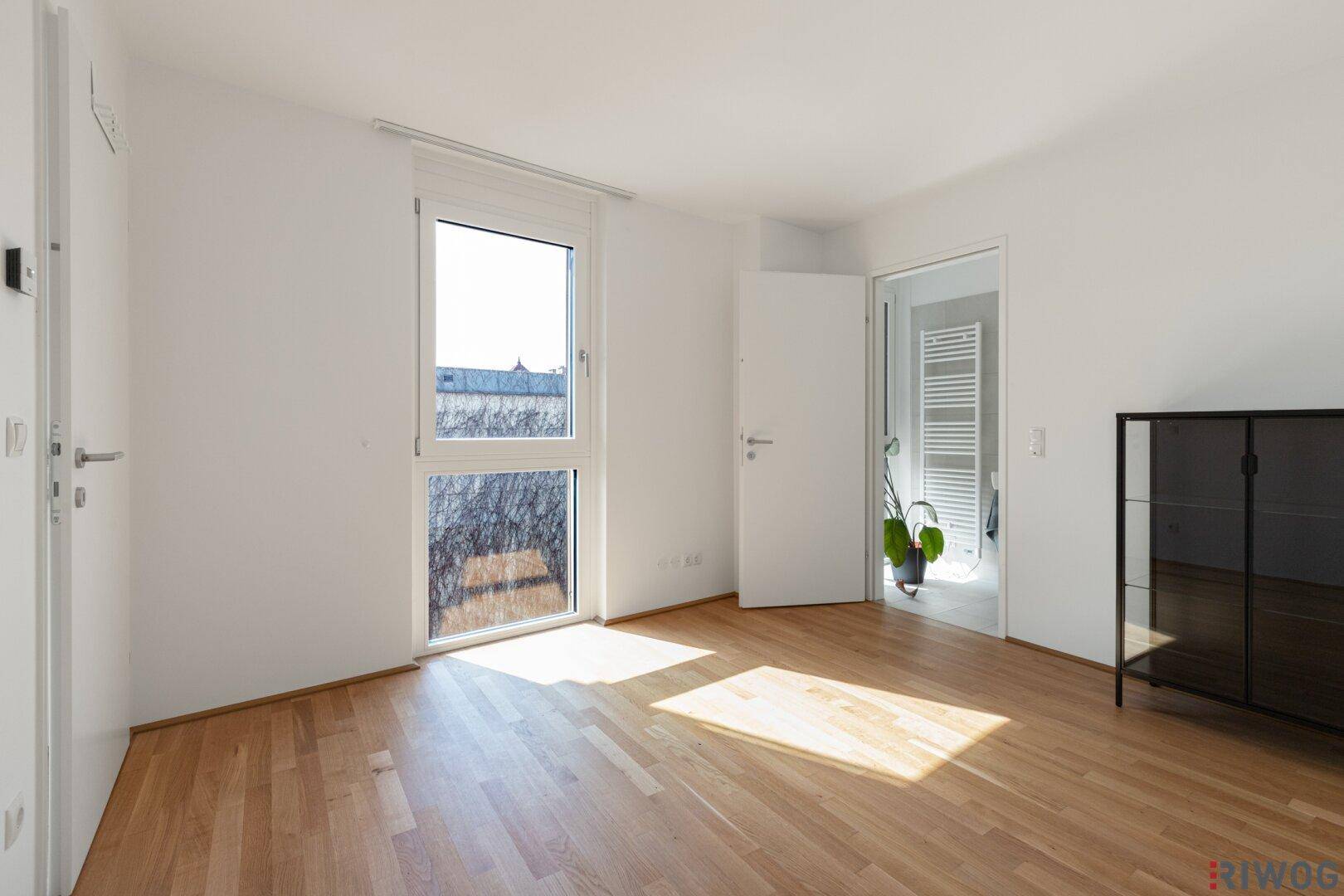 Helles Schlafzimmer mit Holzboden und Fenster, das viel Tageslicht hereinlässt.