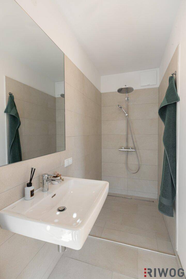 Modernes Badezimmer mit ebenerdiger Dusche, Einzelwaschbecken und großem Spiegel.