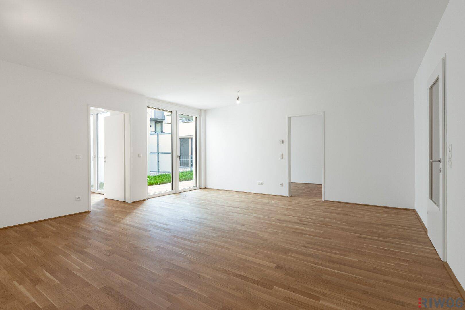 Helles, leeres Wohnzimmer mit Eichenparkettboden und Zugang zu einem kleinen Außenbereich.
