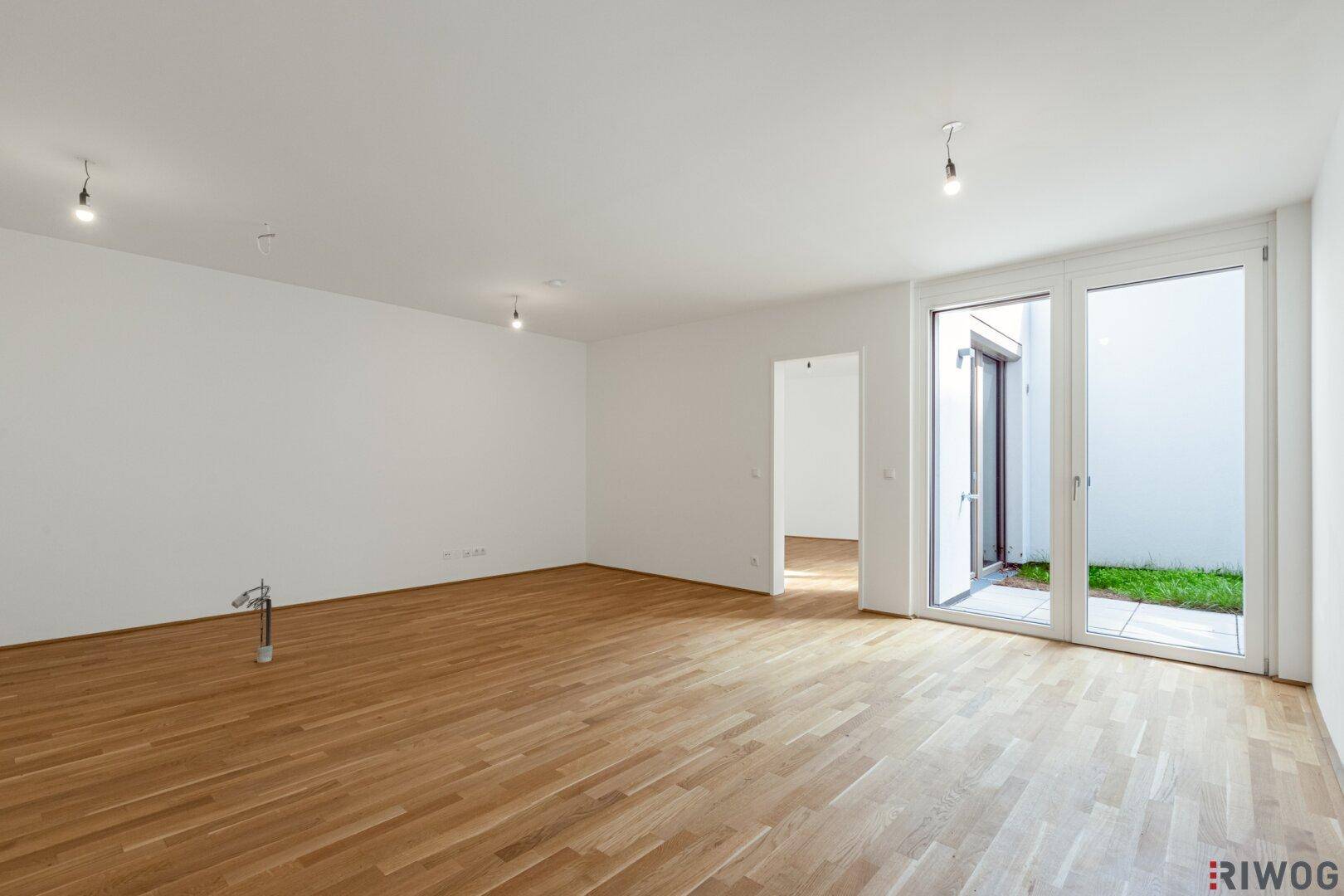 Geräumiges, unmöbliertes Zimmer mit hellem Parkettboden und großen Fenstern zum Außenbereich.