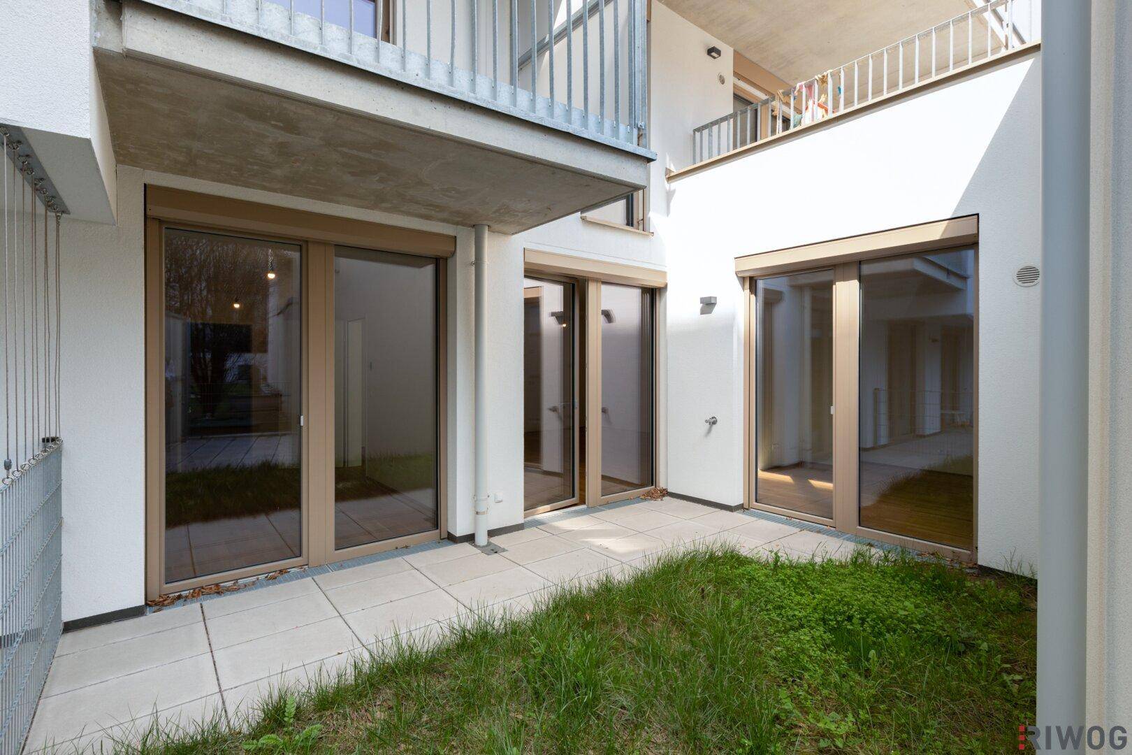 Gepflasterte Terrasse mit angrenzender Grünfläche und Blick auf weitere Gebäudebalkone.