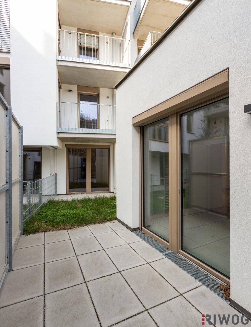 Außenbereich mit gepflasterter Terrasse und kleiner Rasenfläche, umgeben von modernen Gebäuden.