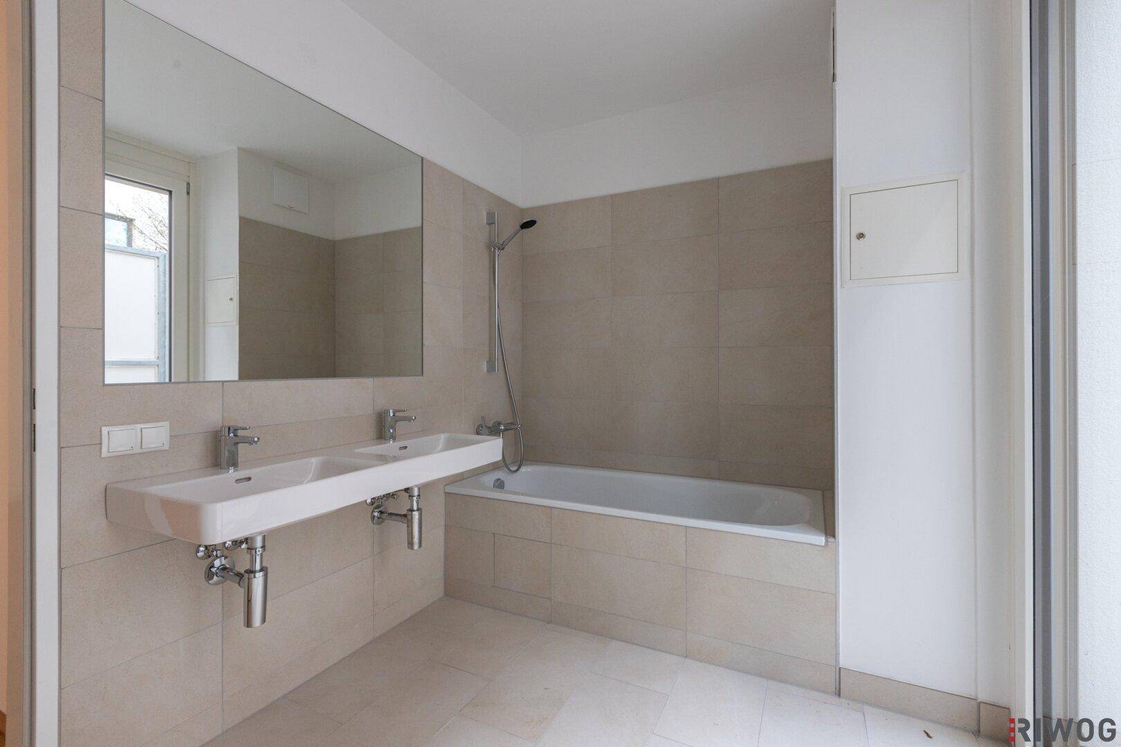 Modernes Badezimmer mit Doppelwaschbecken, Badewanne und großen beigefarbenen Fliesen.