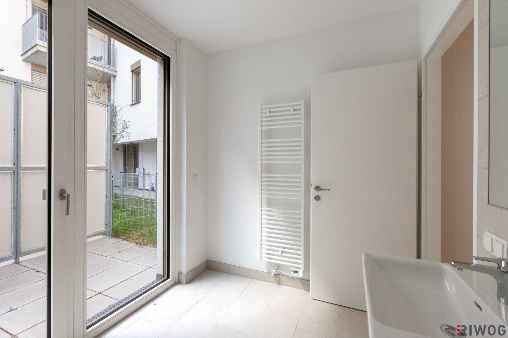 Helles Badezimmer mit Fenster, beheiztem Handtuchhalter und Zugang zu einem Außenbereich.