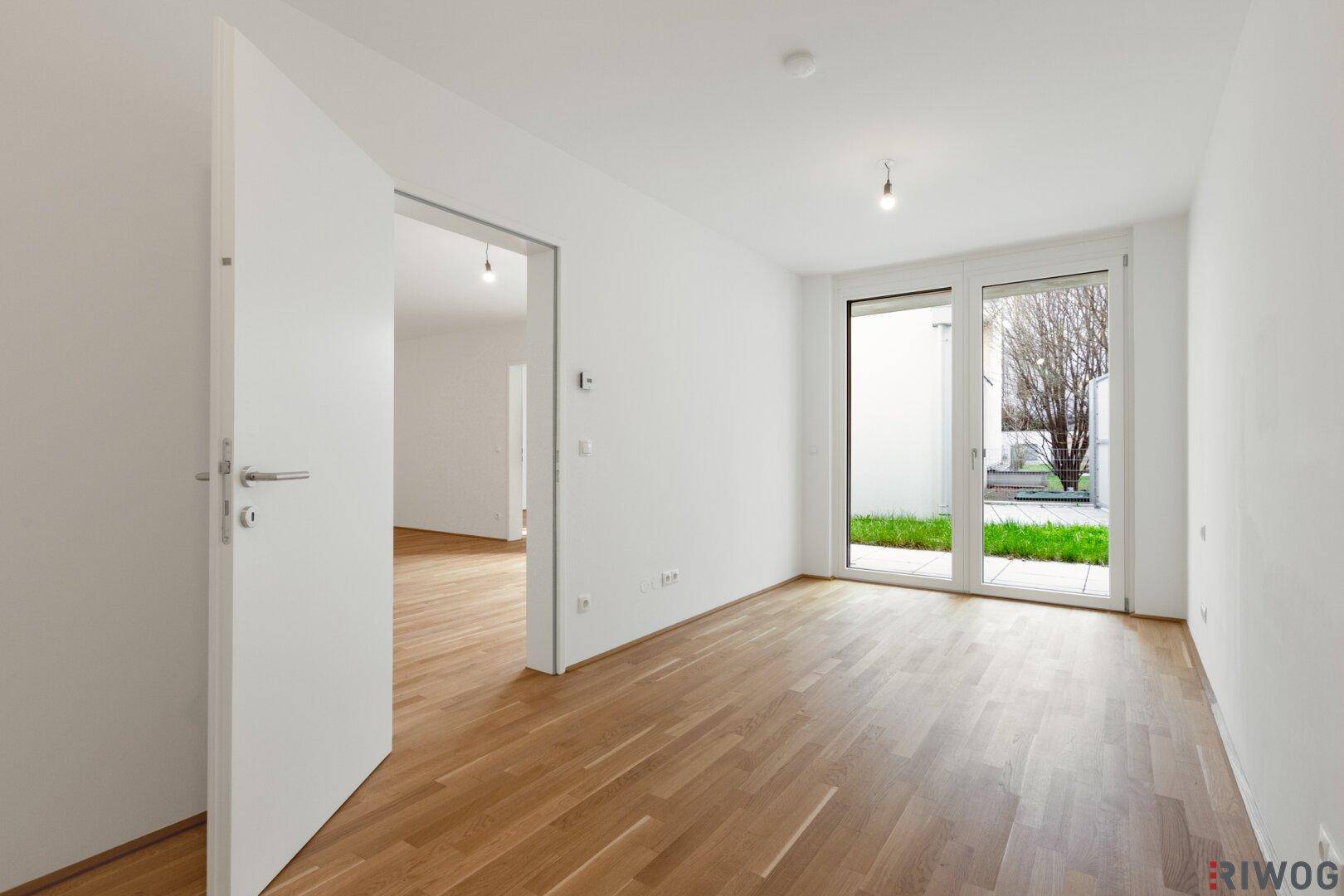 Helles, unmöbliertes Zimmer mit Parkettboden und Zugang zu einem kleinen Außenbereich.
