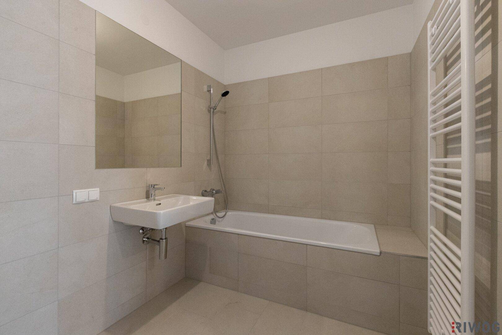 Modernes Badezimmer mit Badewanne, Einzelwaschbecken und beigefarbenen Fliesen.