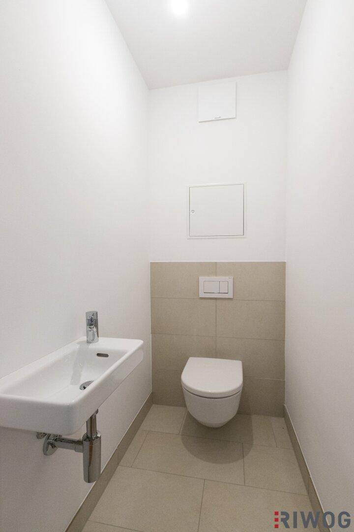 Modernes Gäste-WC mit wandhängender Toilette, kleinem Waschbecken und beigefarbenen Fliesen.