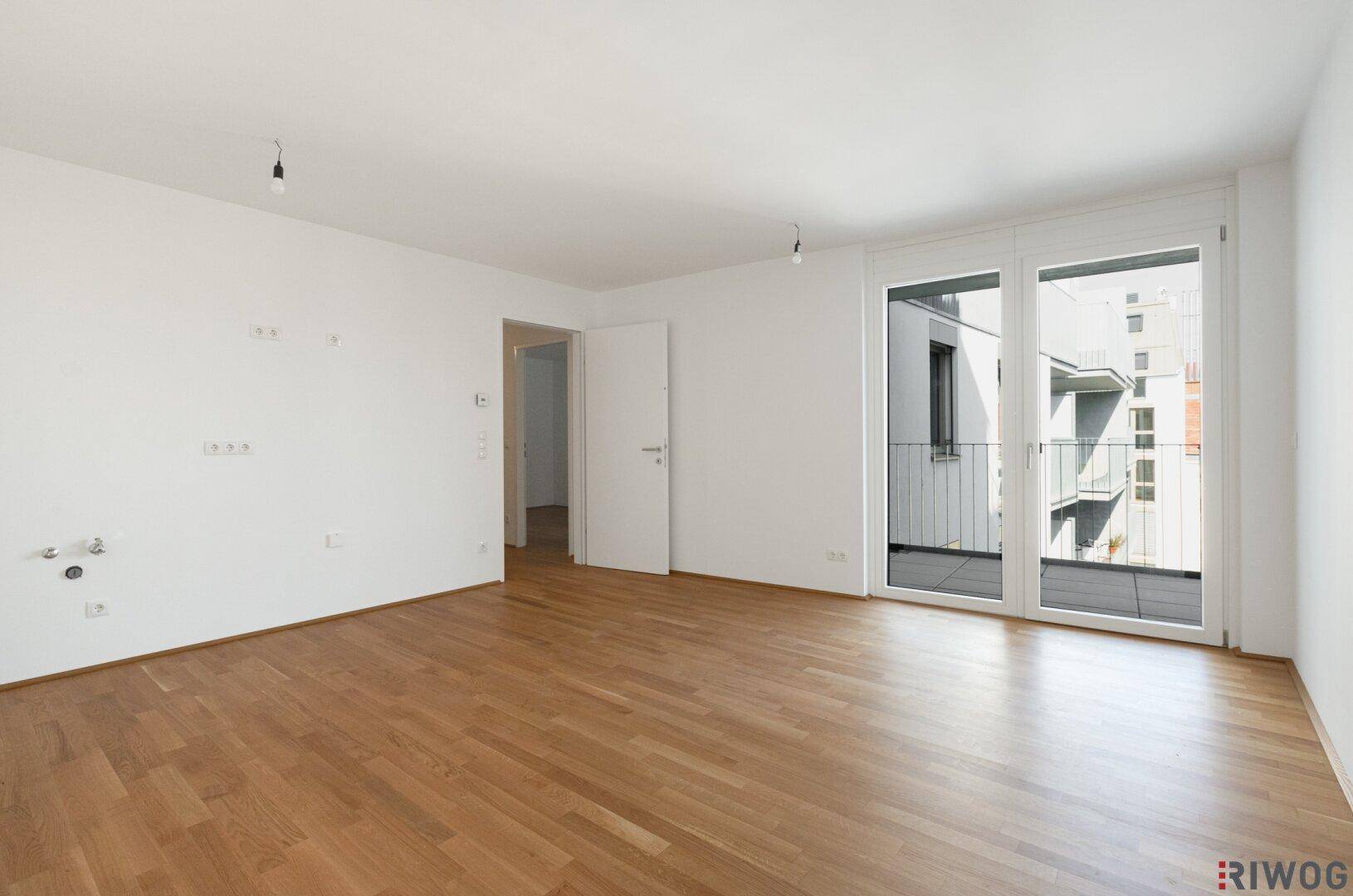 Geräumiges Wohnzimmer mit Parkettboden und Zugang zu einem Balkon.