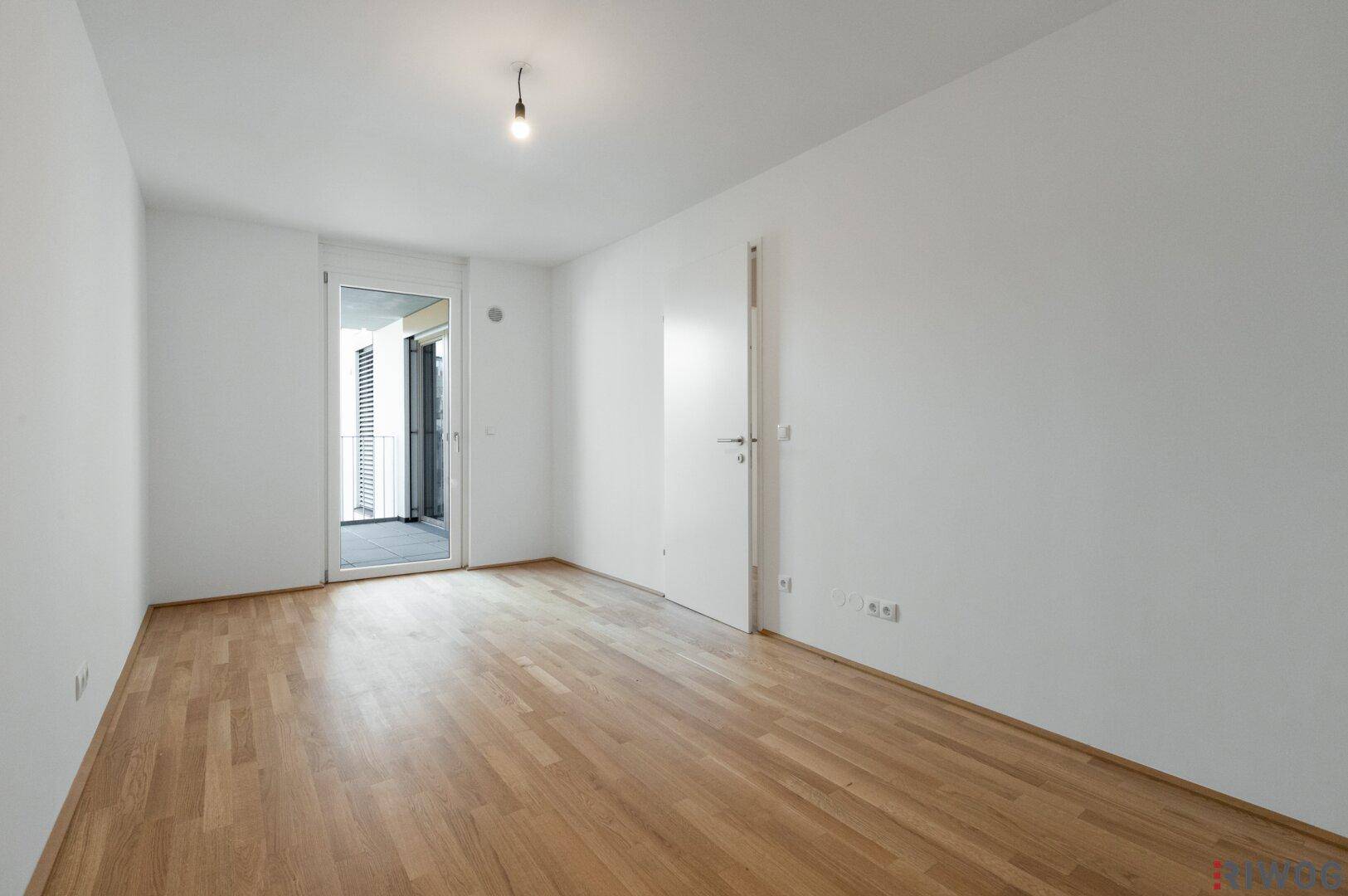 Leeres Zimmer mit Parkettboden und Zugang zu einem Außenbereich.