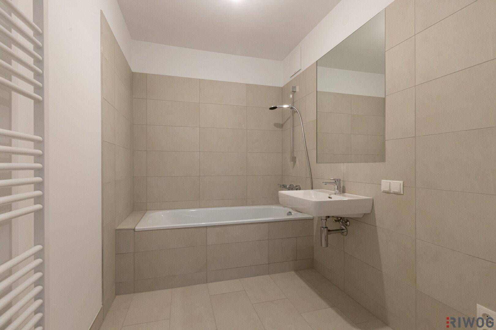 Modernes Badezimmer mit Badewanne, beigefarbenen Fliesen und Wandspiegel.
