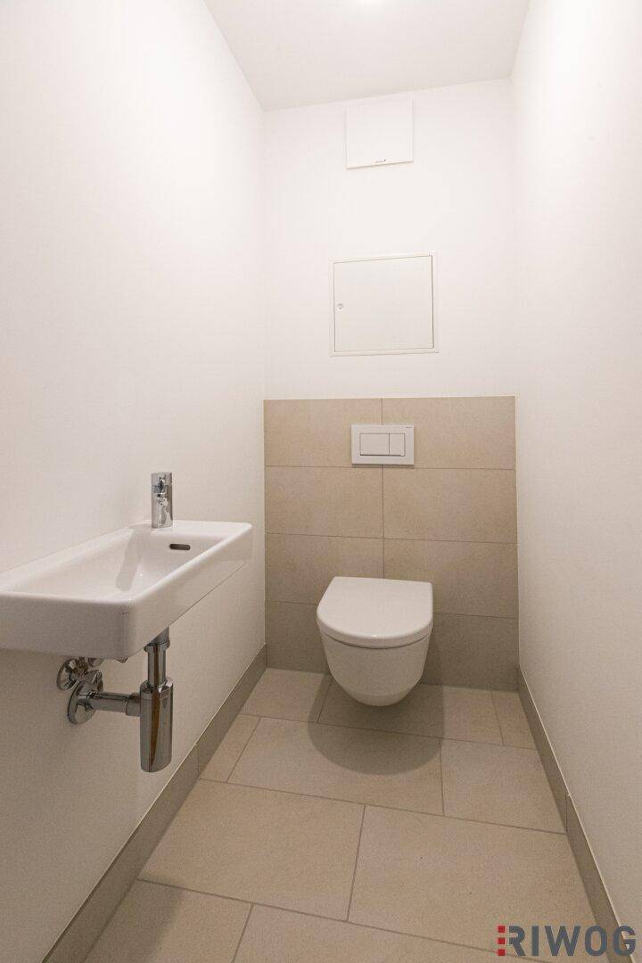 Gäste-WC mit Wand-WC, kleinem Waschbecken und hellen Fliesen.