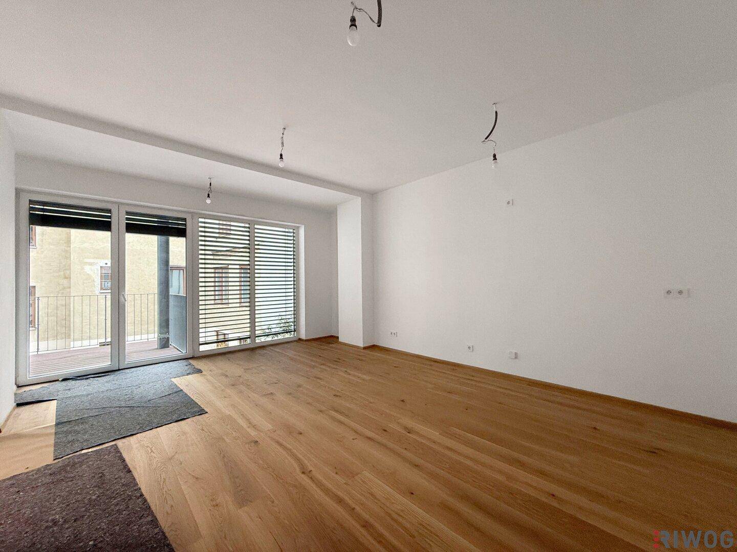 Heller Wohnraum mit neuem Parkettboden und Zugang zu einem Balkon.