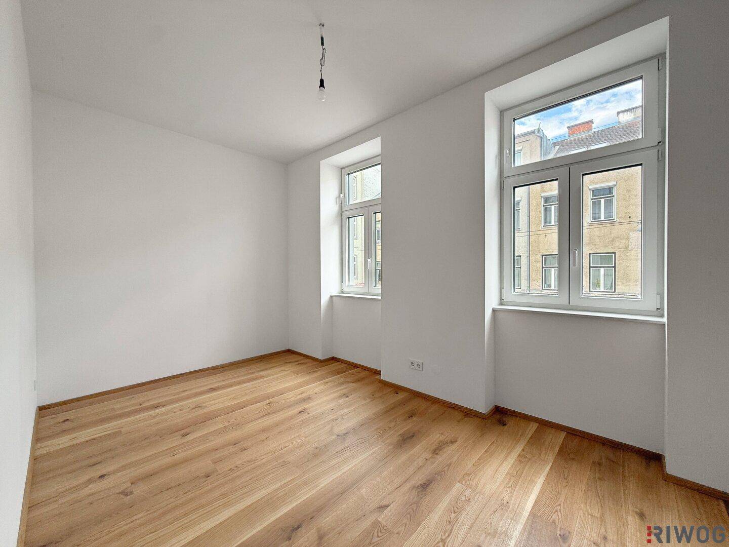 Helles Schlafzimmer mit Parkettboden und zwei großen Fenstern zur Straße.