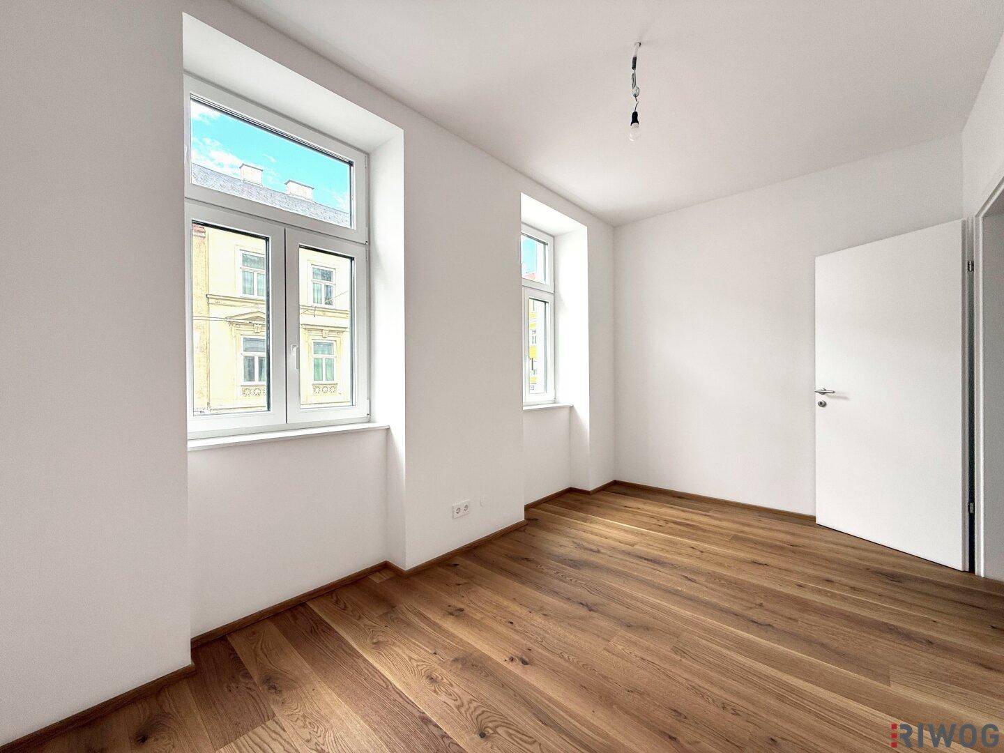 Lichtdurchflutetes Zimmer mit Holzboden und weiß gestrichenen Wänden.