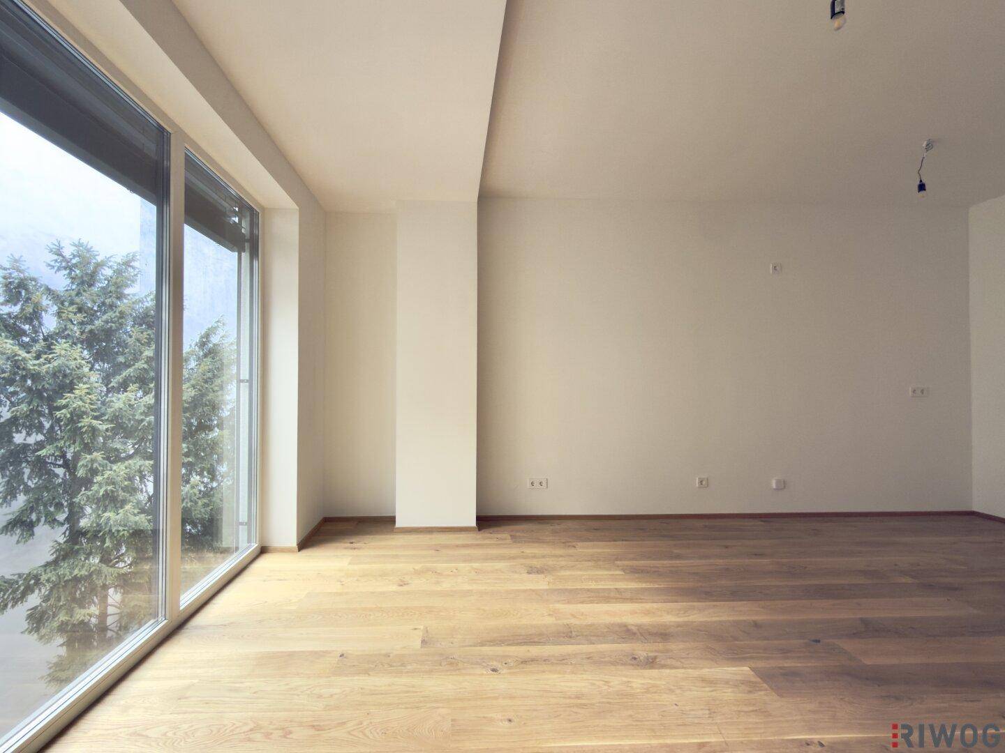 Helles, leeres Zimmer mit großen Fenstern und Holzboden, bereit für die individuelle Gestaltung.