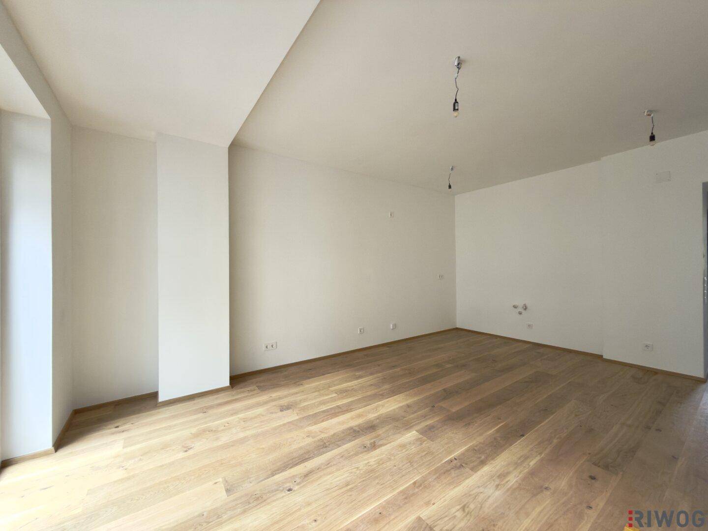 Geräumiges, leeres Zimmer mit hellem Holzboden und weißen Wänden, ideal für Wohnzwecke.