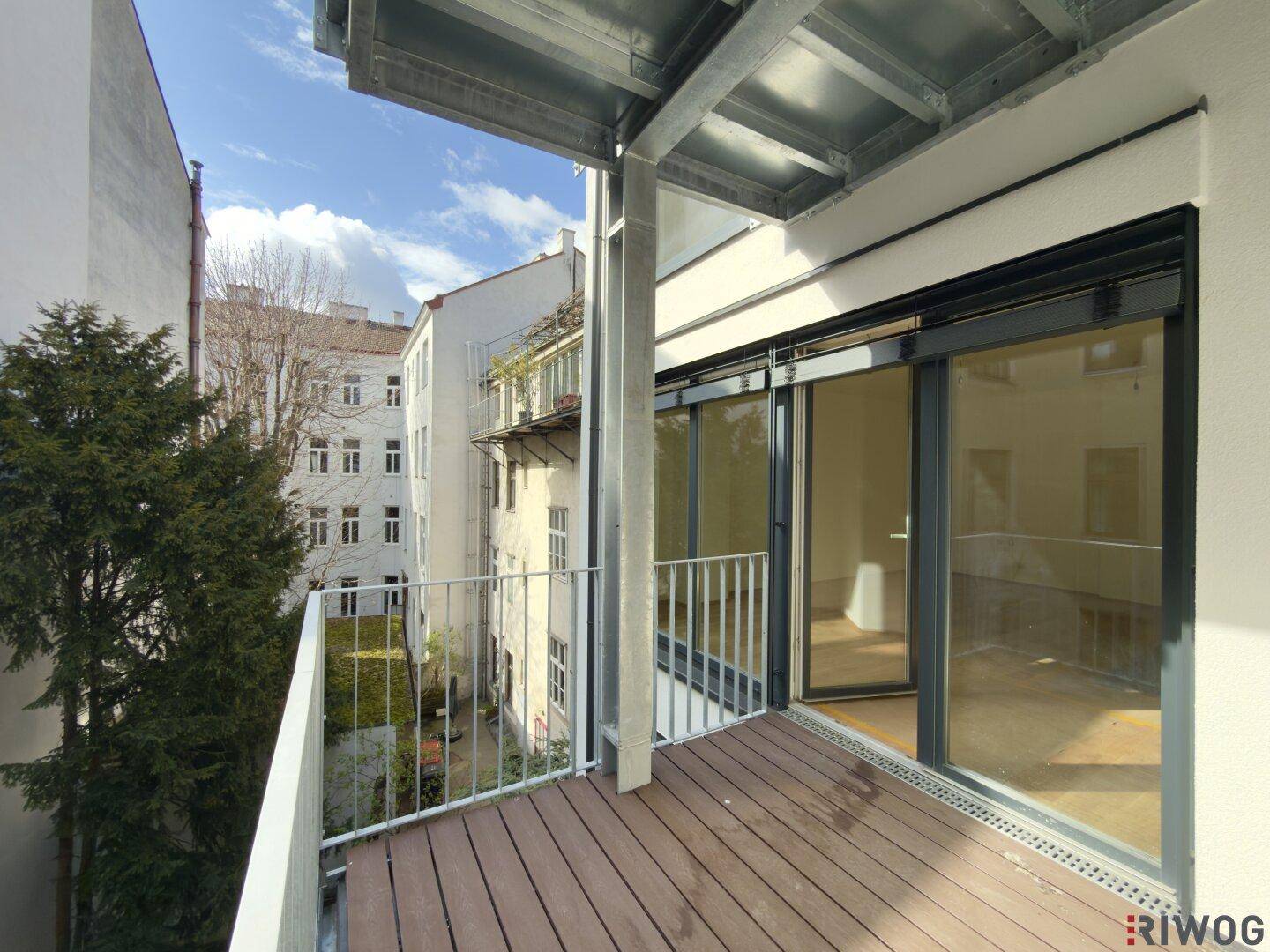 Moderner Balkon mit Holzdielen und Blick auf den Innenhof, ideal zum Entspannen.