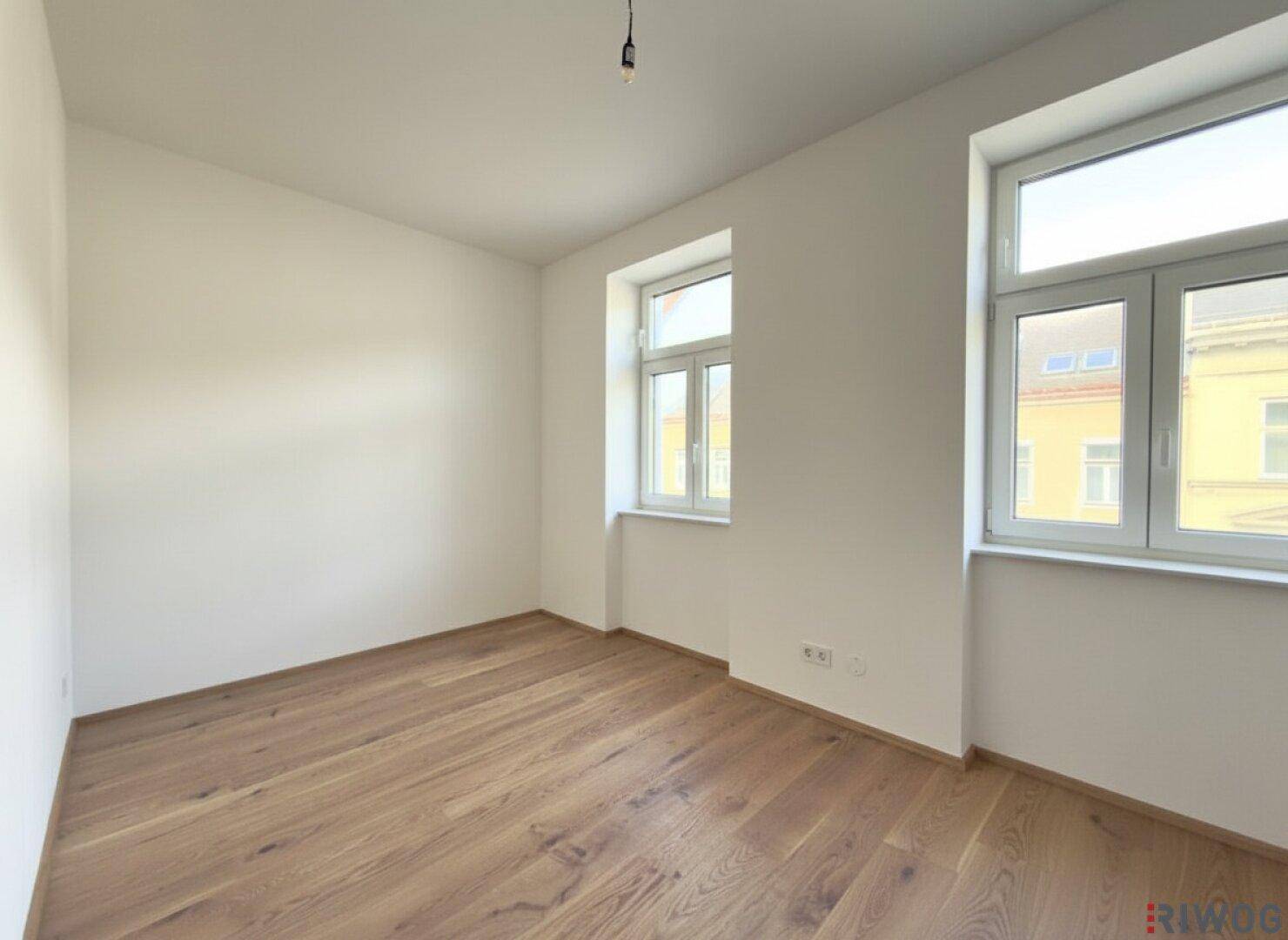 Helles Schlafzimmer mit zwei Fenstern und Parkettboden, bietet eine ruhige Atmosphäre.