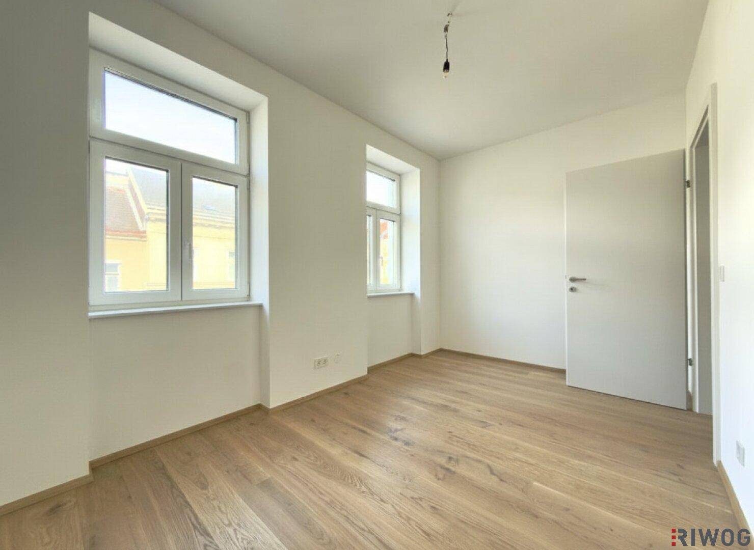 Geräumiges Schlafzimmer mit zwei Fenstern und Holzboden, ideal für erholsame Nächte.