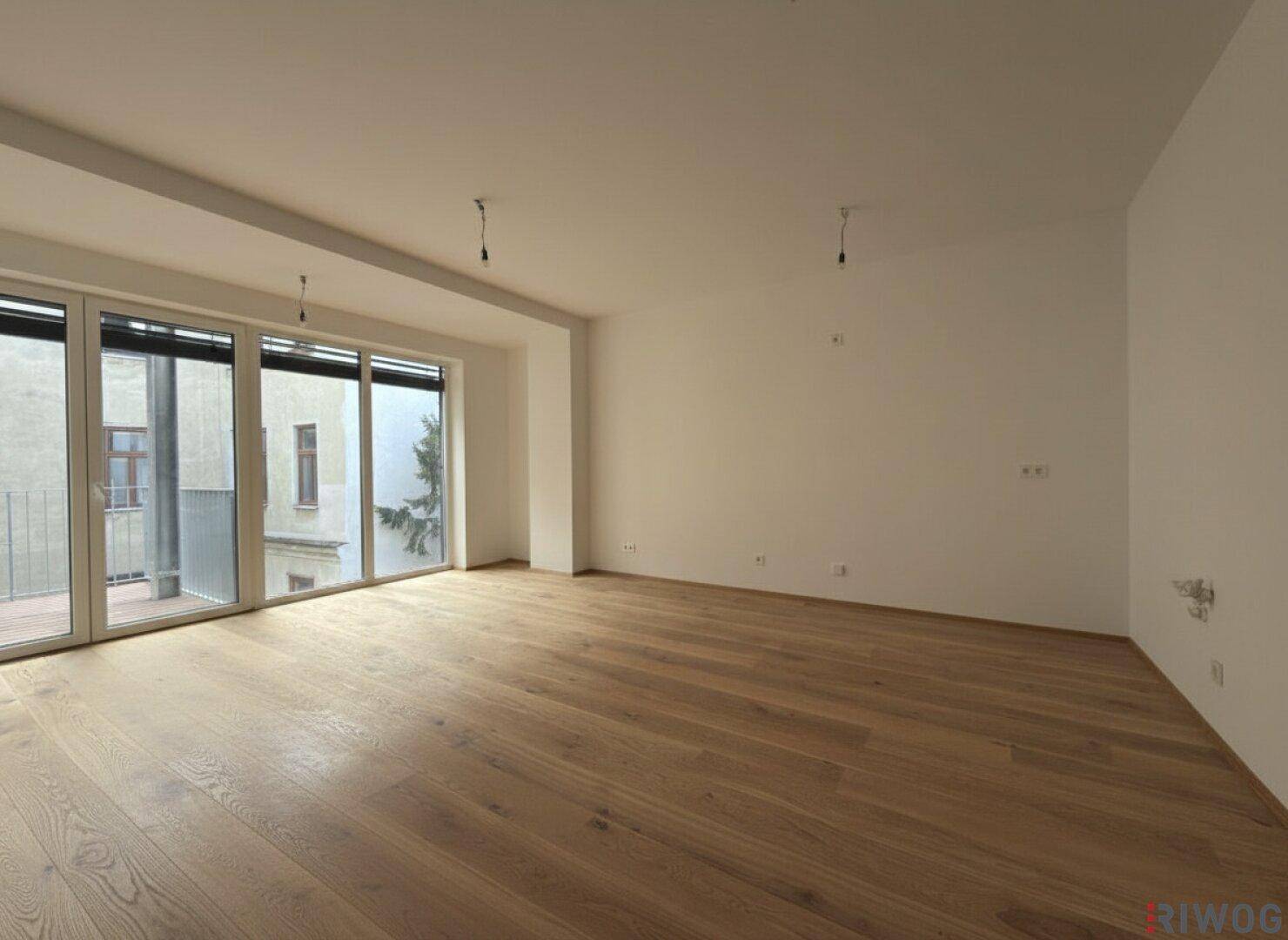 Heller Wohnbereich mit großen Schiebetüren zum Balkon und neuem Parkettboden.