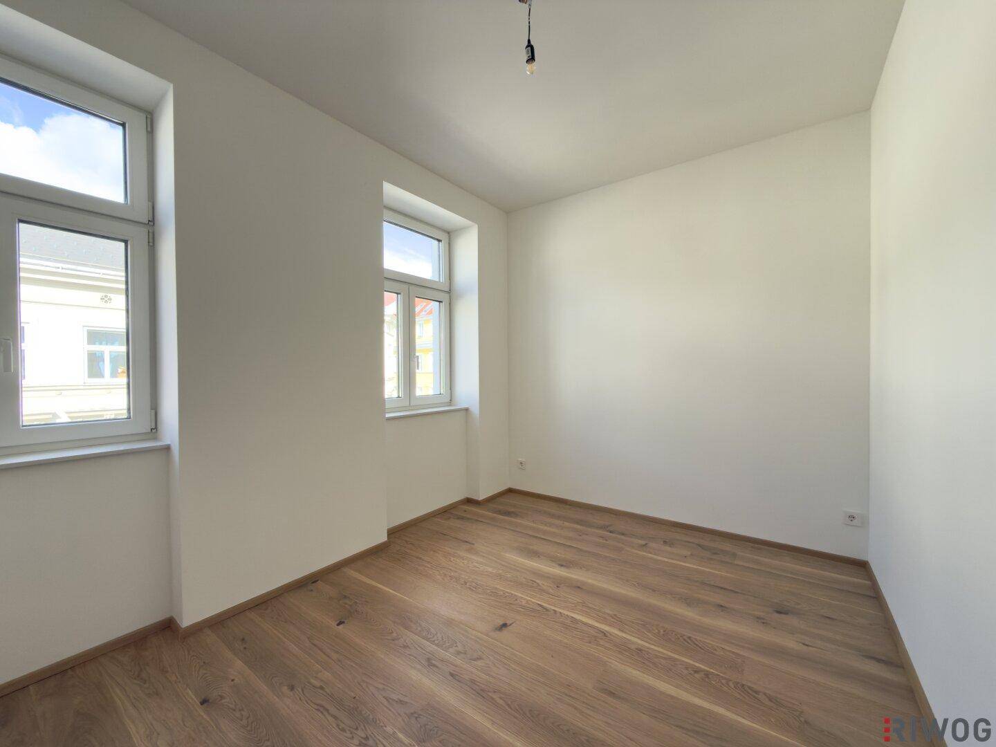 Lichtdurchflutetes Zimmer mit zwei Fenstern und hochwertigem Holzparkett, ideal als Schlafzimmer.